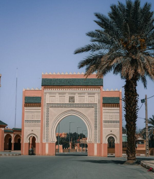 Beautiful Moroccan archway in Rissani with palm trees under a clear blue sky.