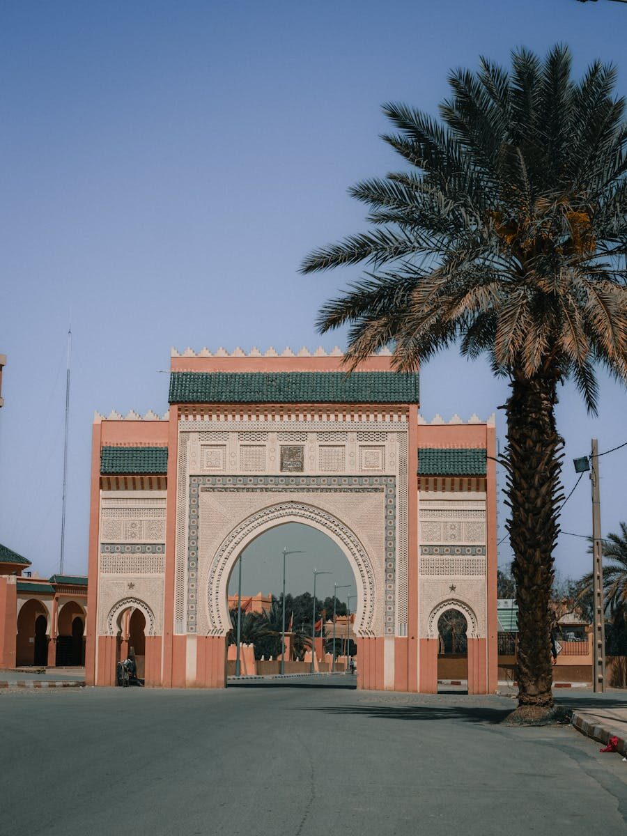 Beautiful Moroccan archway in Rissani with palm trees under a clear blue sky.