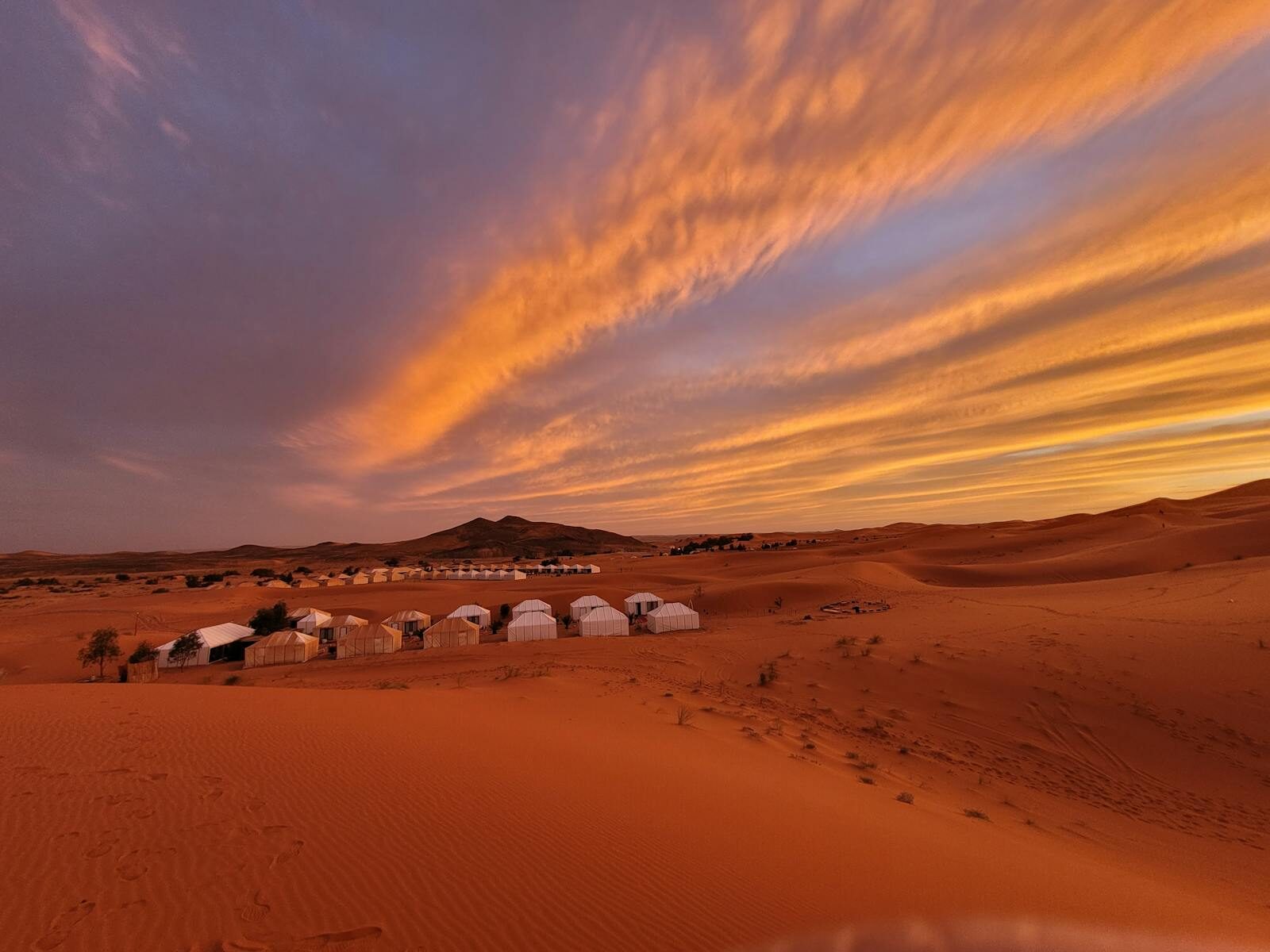 White tents in the Sahara Desert under a dramatic orange and blue sunset sky.